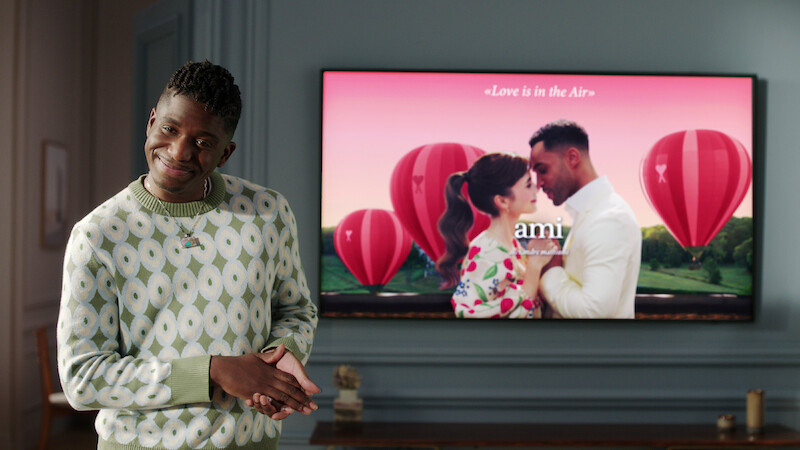 Samuel Arnold as Julien in Emily in Paris stands in front of a presentation on a screen in an office in Season 4 of 'Emily in Paris'