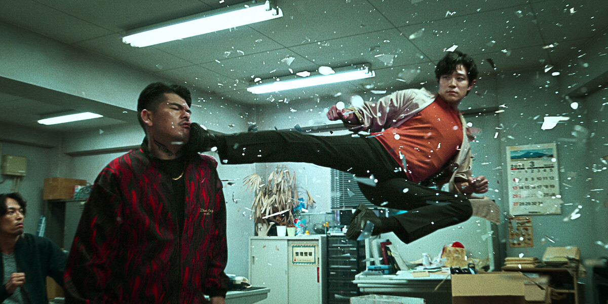 In an image from the film ‘City Hunter,’ actor Ryohei Suzuki as Ryo Saeba kicks a man in the face while suspended in midair in an office.