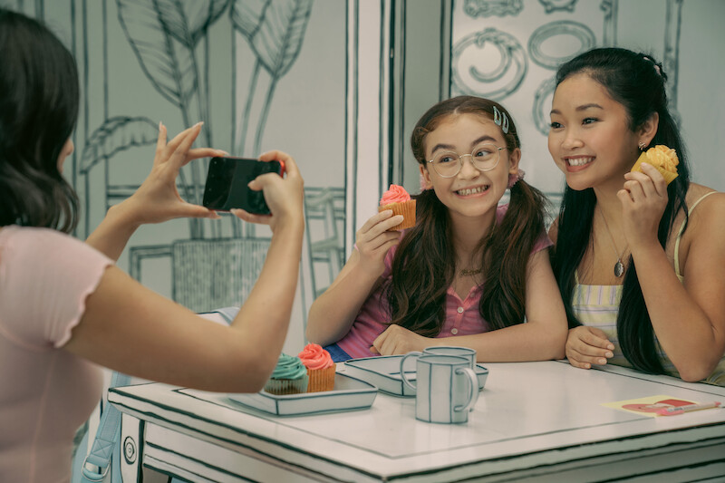 Anna Cathcart as Kitty, Lana Condor as Lara Jean, and Janel Parrish as Margot take pictures at a cafe.