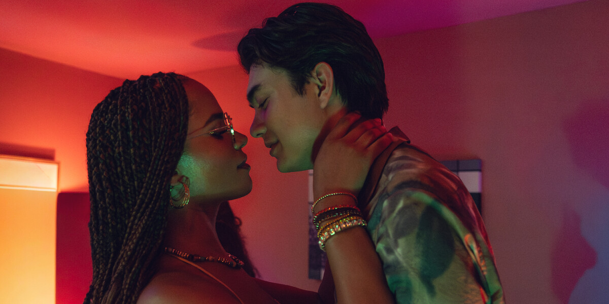 Two people in an intimate pose in a dimly lit room with colorful lighting, facing each other closely, creating a romantic atmosphere.