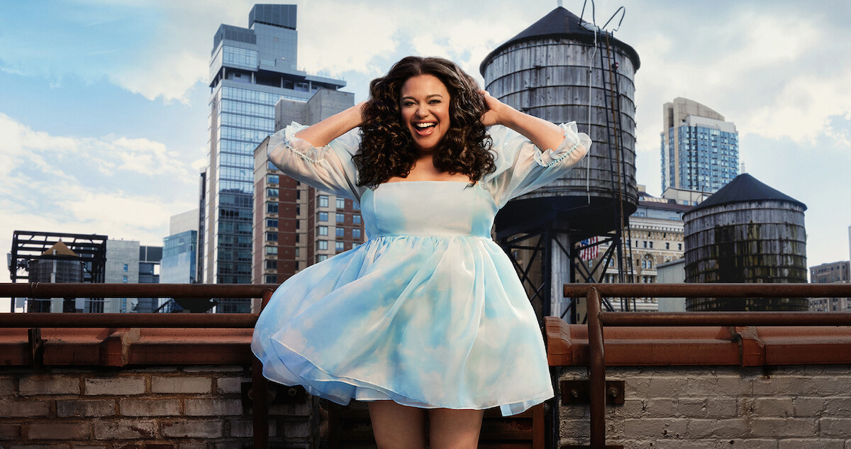 Michelle Buteau wears a bright, patterned jacket and laughs.
