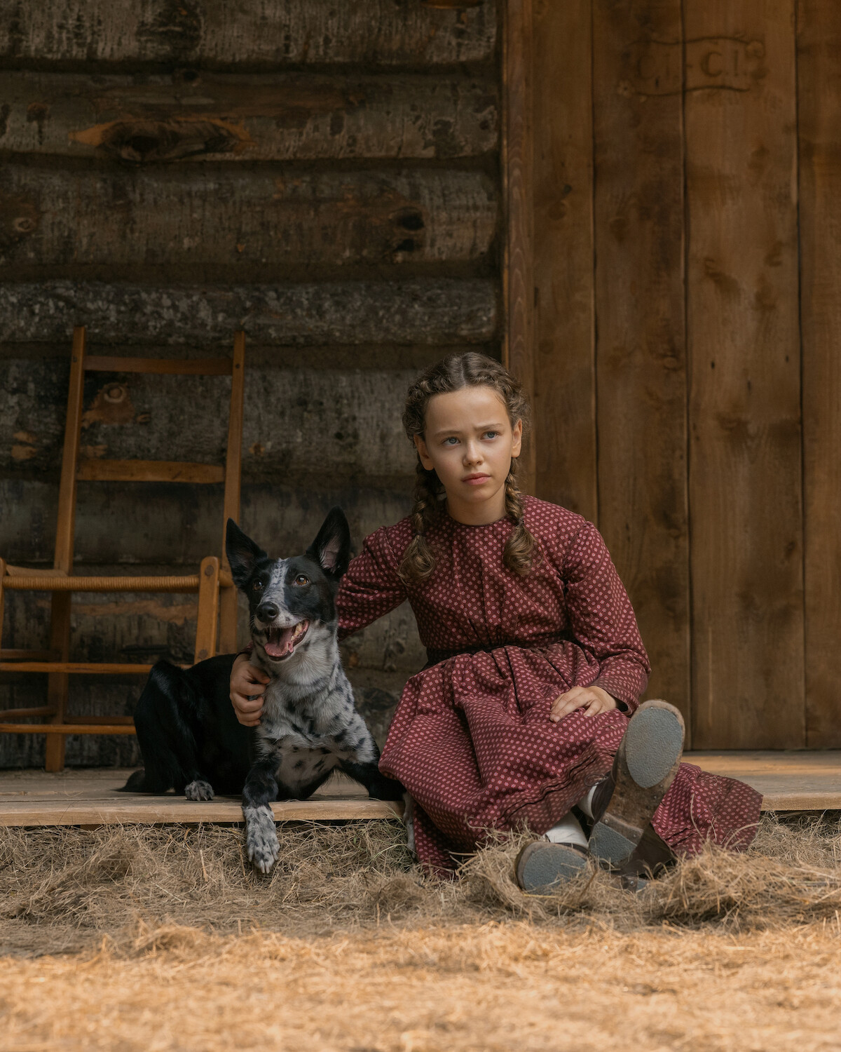 A dog sits next to a young girl on a porch.