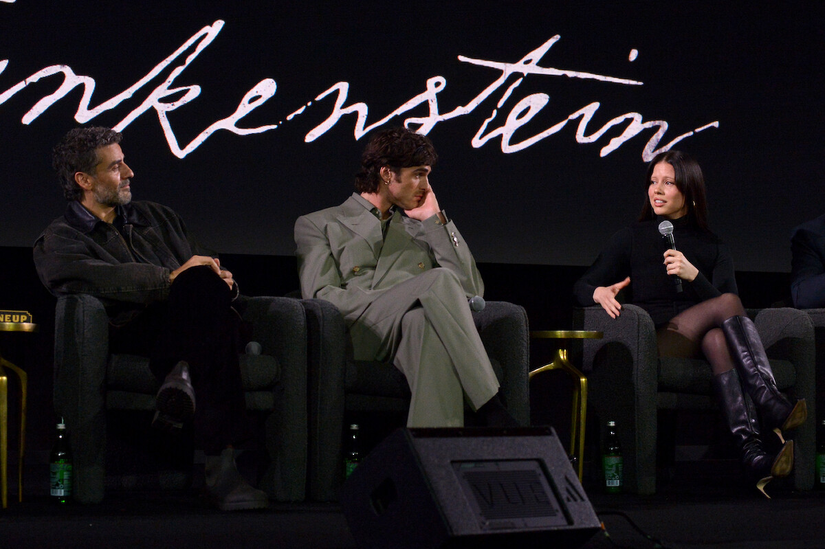 Oscar Isaac, Jacob Elordi, and Mia Goth hold mics as they speak on a panel.