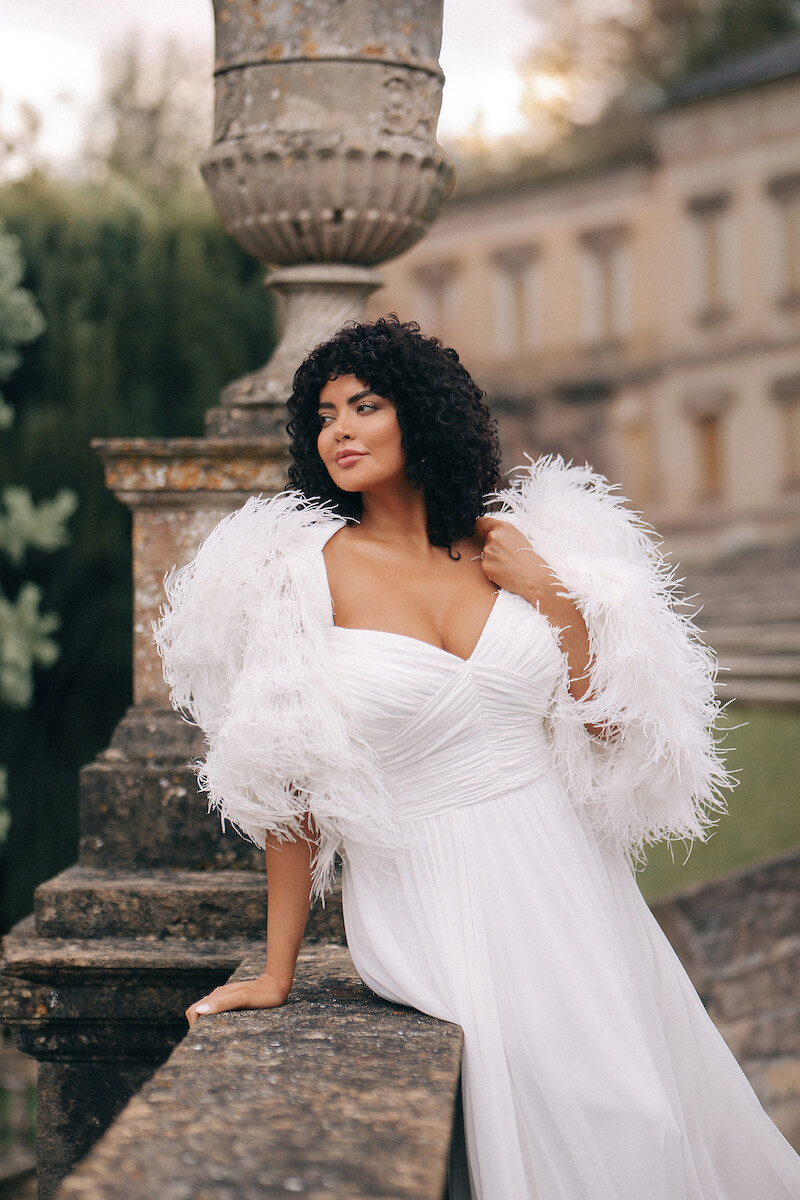 Woman in bridal dresses poses and looks off into the distance.