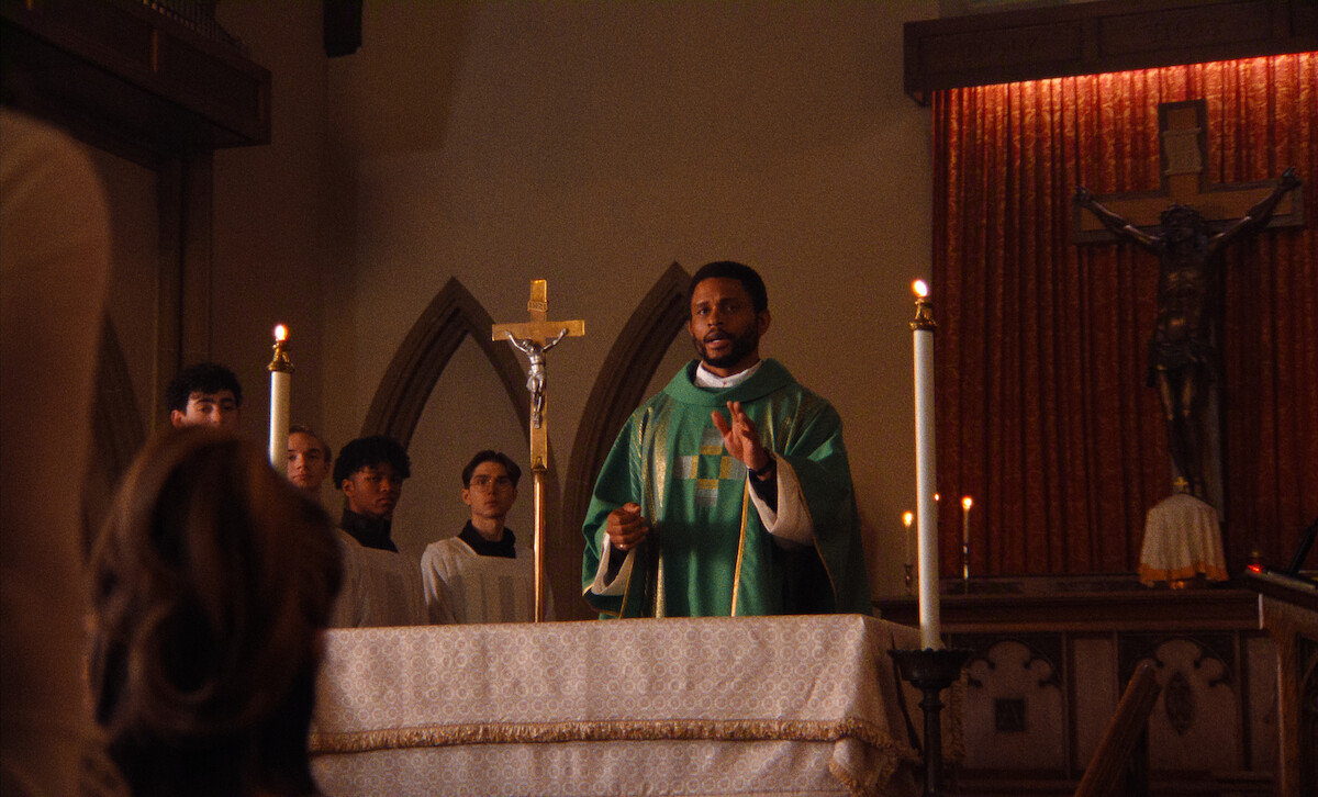 A priest in green vestments leads a church service at the altar, with altar servers behind him, candles and a crucifix present, and congregants visible in the foreground within a dimly lit sanctuary.