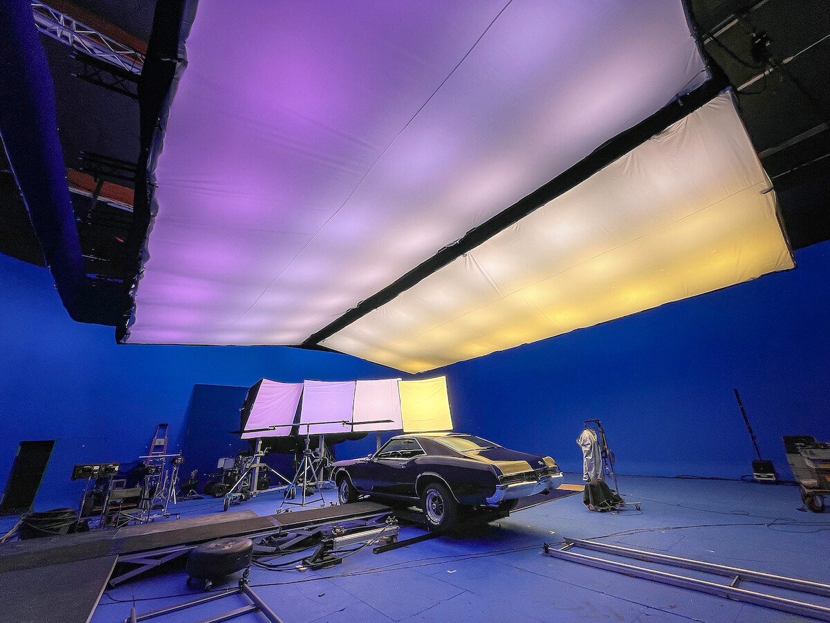 Behind the scenes of the dramatic final car chase scene. A black car rocks back and forth in a purple, yellow, blue room.