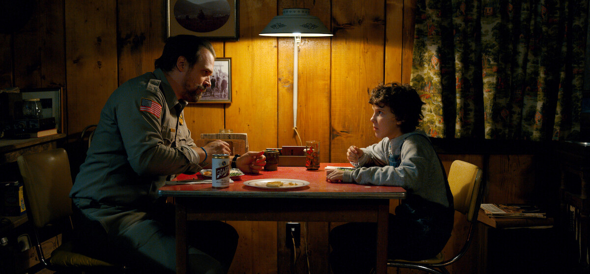 Hopper and Eleven sitting across from each other at a dinner table.
