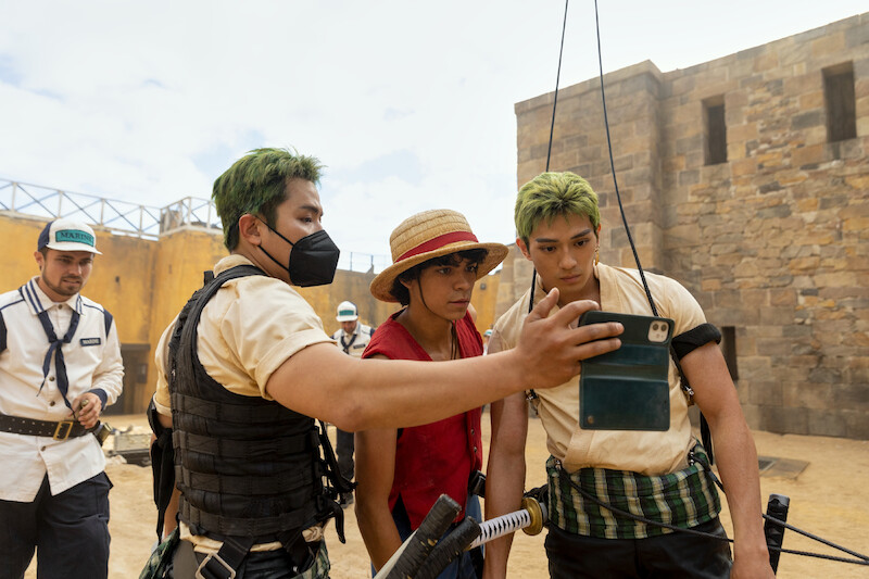 Stunt double/katana specialist Koji Kawamoto, Iñaki Godoy as Monkey D. Luffy, and Mackenyu as Roronoa Zoro look at a phone together in Season 1 of 'One Piece.'