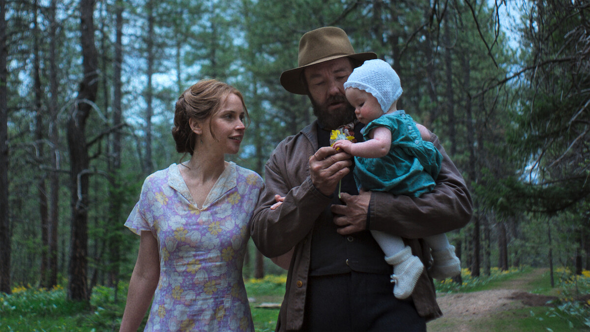 Felicity Jones as Gladys and Joel Edgerton as Robert Grainier holding a child as they walk through the forest.