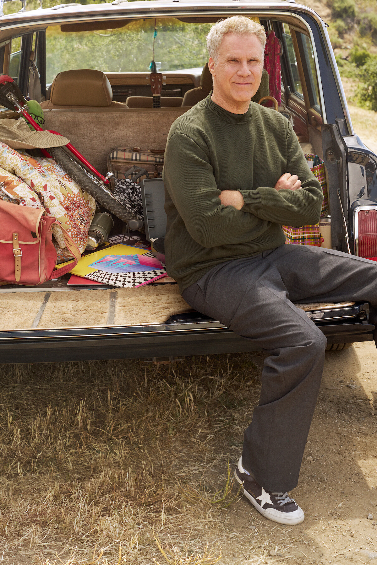 Will Ferrell sits in the back of a car wearing a green sweater.