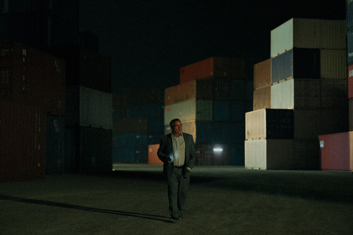 Eduardo Fernández as Joaquín Manchado walks in a shipping container yard at night in a still image from Season 1 of ‘Iron Reign.’