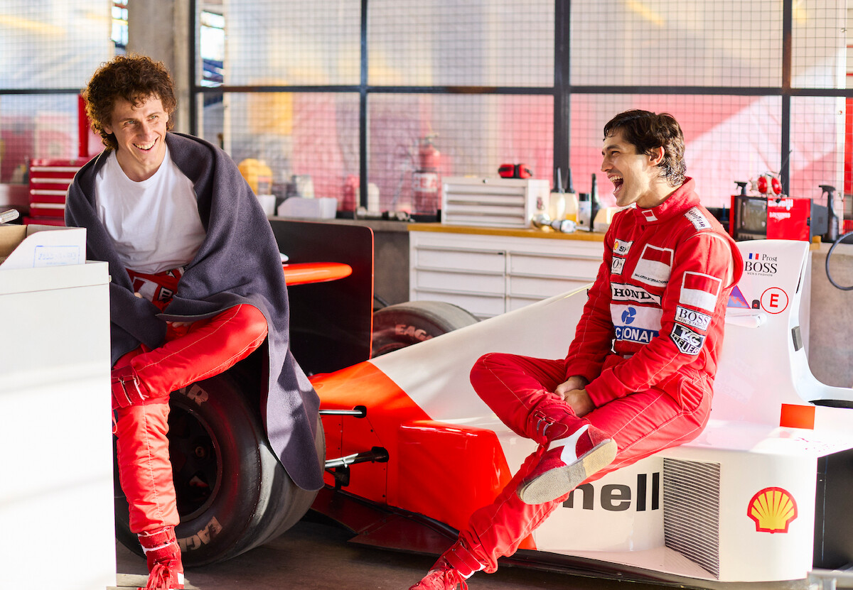 Alain Prost (Matt Mella) and Ayrton Senna (Gabriel Leone) have a grand old time on set. Both boys laugh, and Mella wears a gray blanket as a shawl.