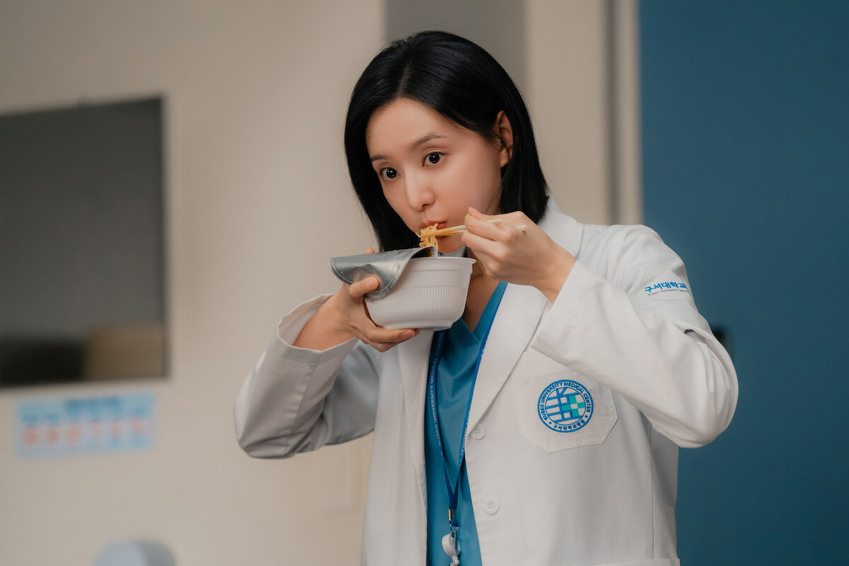Uma mulher sul-coreana de cabelos pretos come usando um bowl e um par de hashis