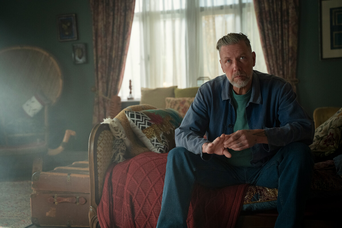 Mikael Persbrandt as Jakob Nyman sits on a sofa in Season 3 of ‘Sex Education.’