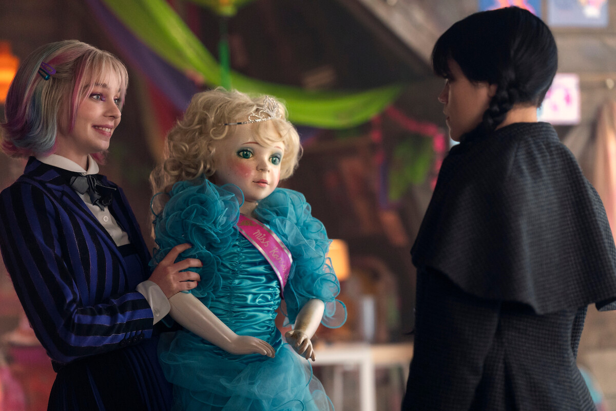 Emma Myers as Enid Sinclair holds a doll and smiles at Jenna Ortega as Wednesday in Season 2 of ‘Wednesday’