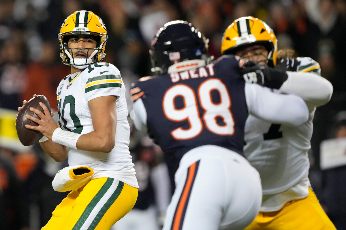 Green Bay Packers quarterback looks to throw as Chicago Bears defender rushes, Packers offensive lineman blocks during a night NFL football game in a stadium full of fans.