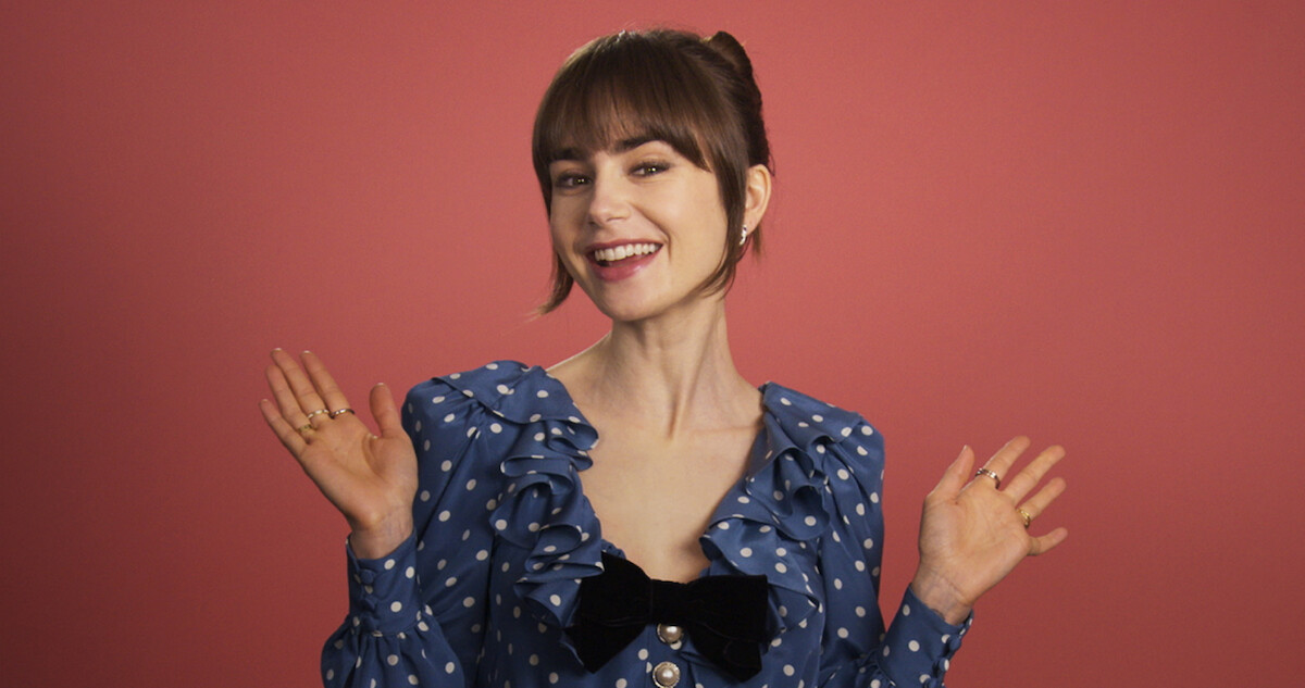 Lily Collins smiles wearing a blue dress with white polka dots