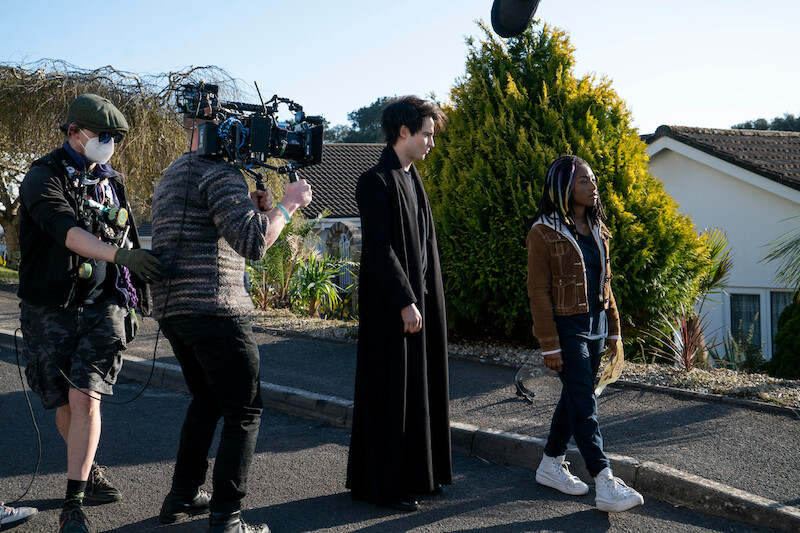 Morpheus (Tom Sturridge) and Rose Walker (Vanesu Samunyai) film a dream sequence on a suburban street.