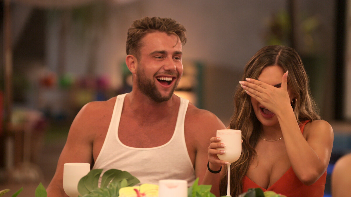 Harry laughs while Jessica is holding a drink and covering her face.