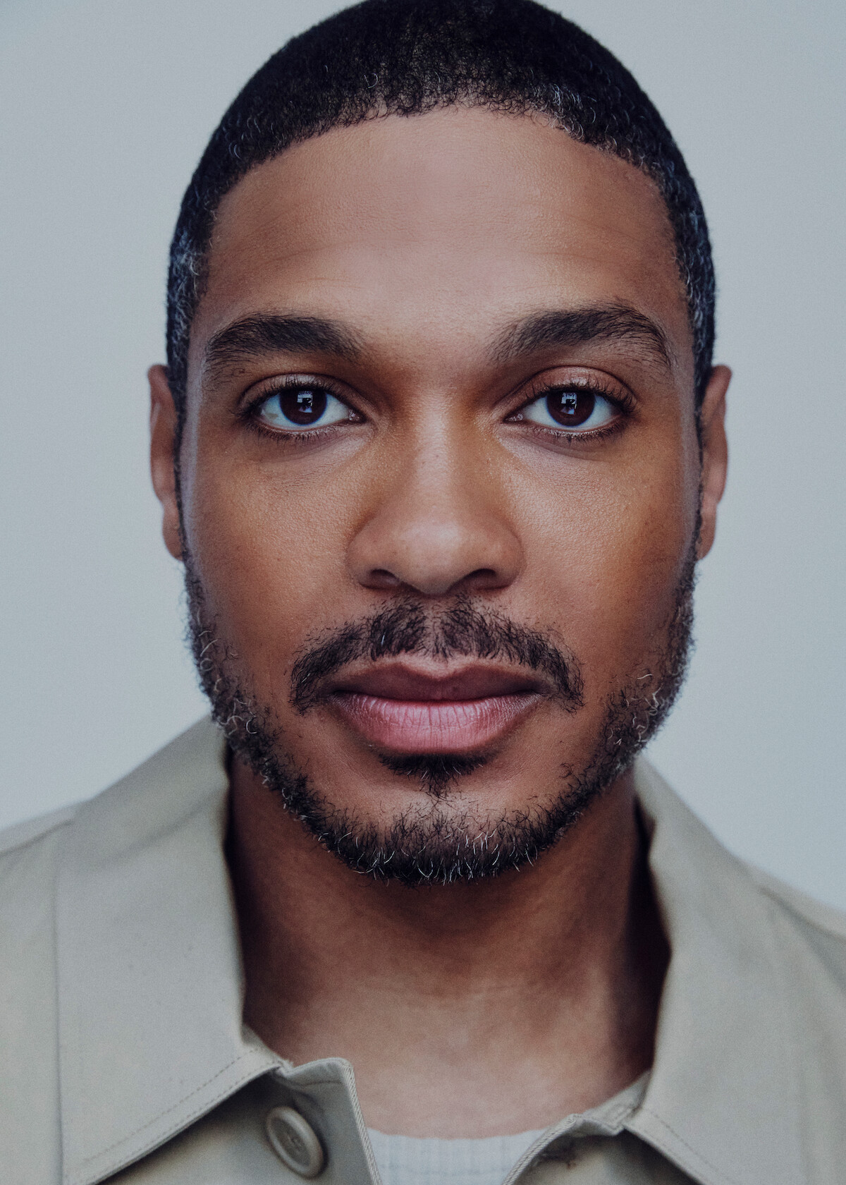 Ray Fisher wears a tan jacket and stares at the camera.