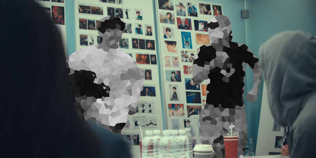 People gathered in a meeting room with a wall covered in photographs, water bottles on the table, some individuals are pixelated for privacy.