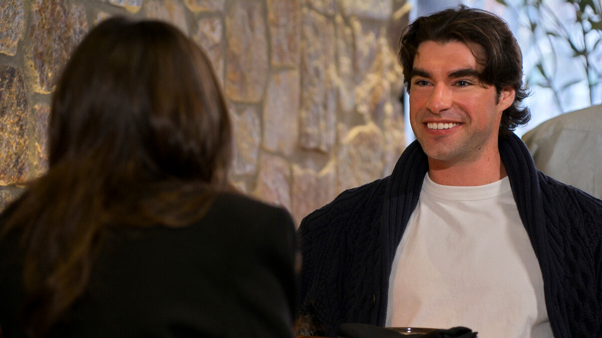 A man smiling across a table from a woman in a casual indoor setting with stone walls, suggesting a relaxed conversation or meeting at a cafe or restaurant.
