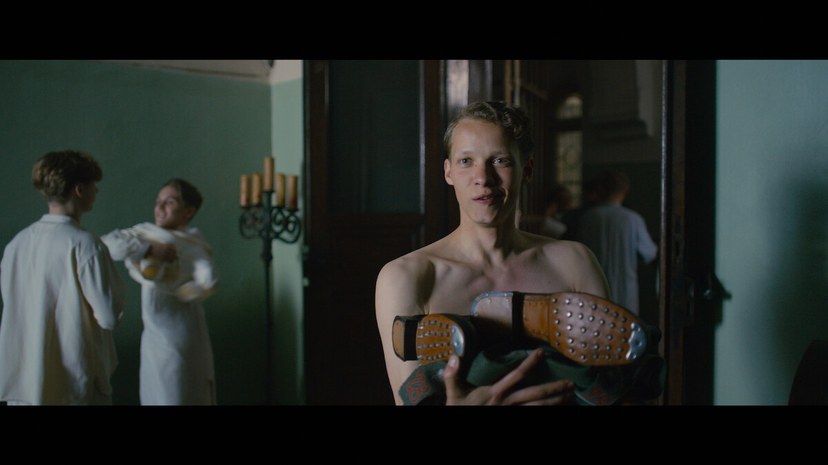 Protagonist Paul Bäumer holds nail-studded boots in his arms.