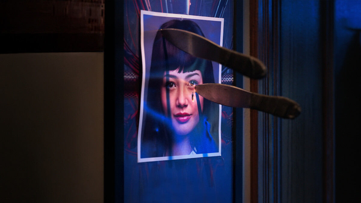 A photo of Miku Martineau with two knives stabbed into it hangs from a wall in an image from the series ‘Bet.’