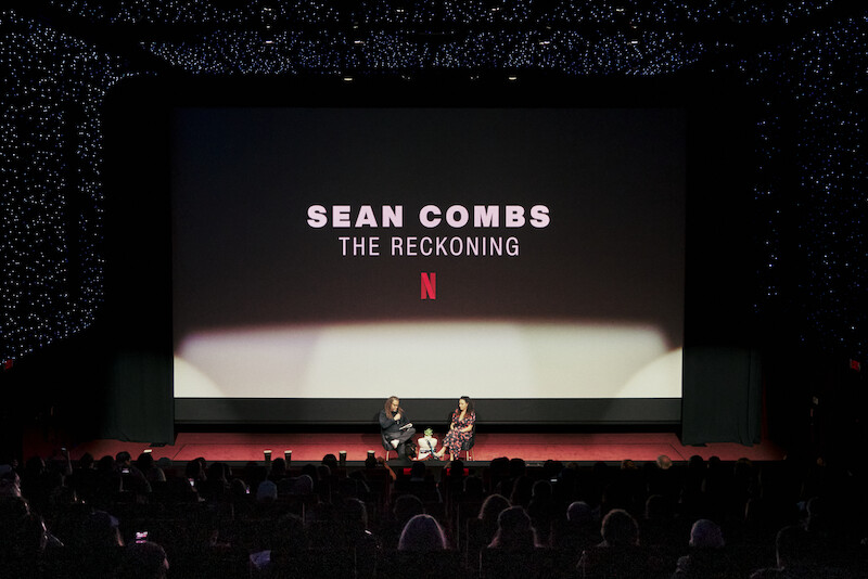 A theater with a stage with two people in chairs sitting on it.