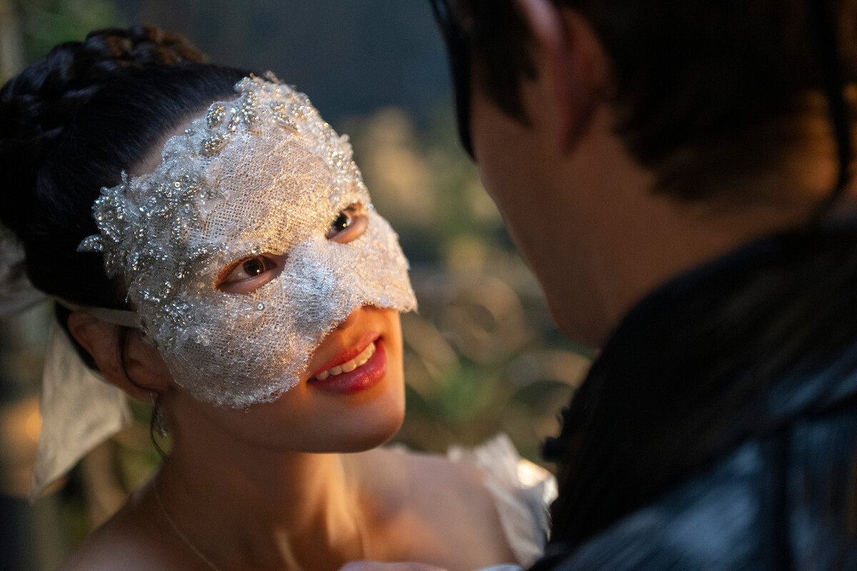 Woman in a decorative white lace mask smiling at a man in black attire at a masquerade ball, soft background lighting, romantic atmosphere.