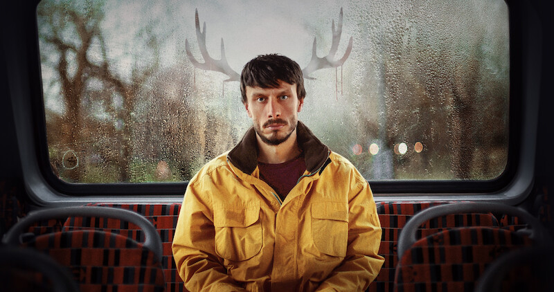 Richard Gadd as Donny Dunn sits in the back of a bus with reindeer antlers outside, behind his head in Season 1 of 'Baby Reindeer'