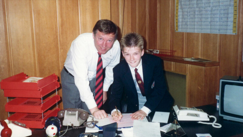 A young David Beckham with his father behind a desk