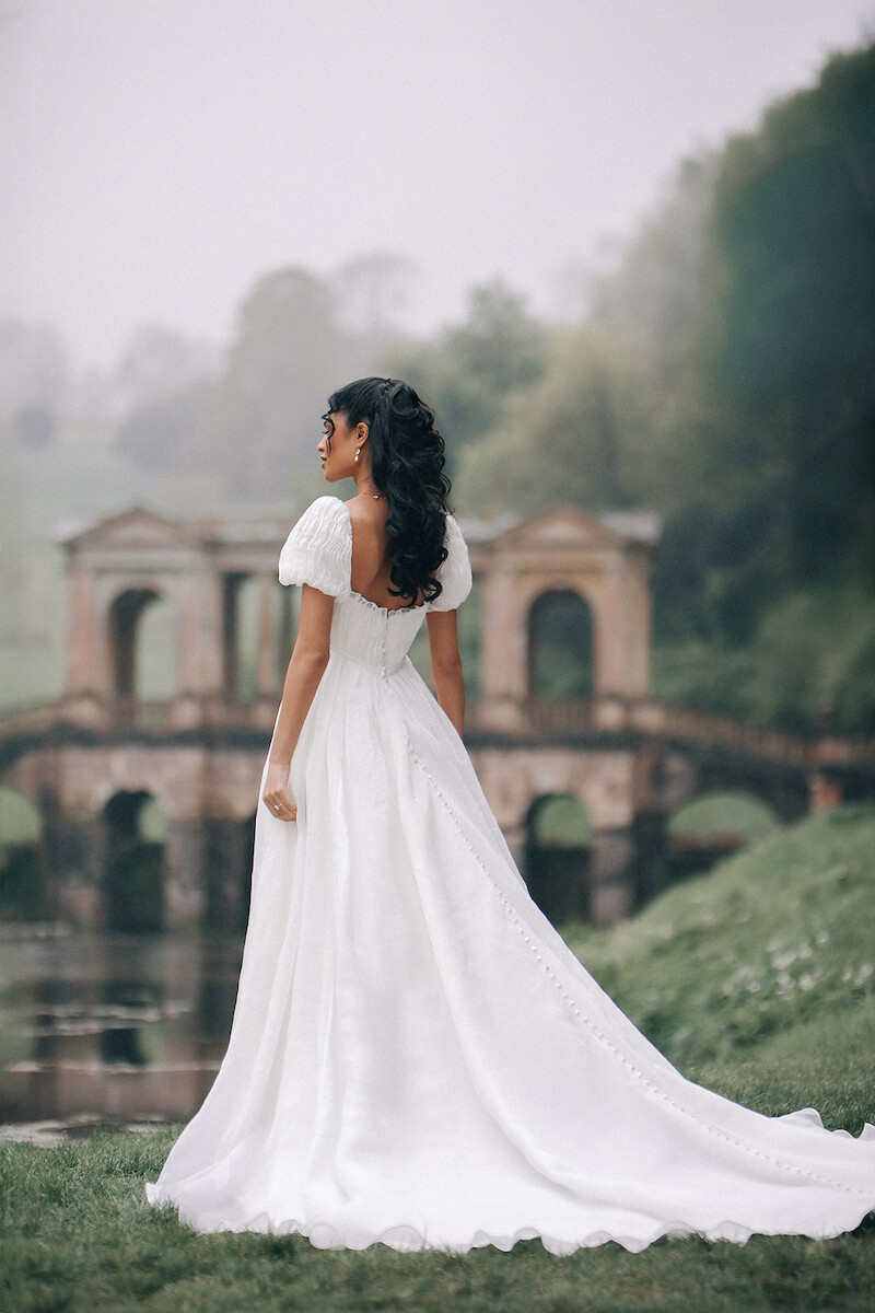 Woman in bridal dresses poses and looks off into the distance.