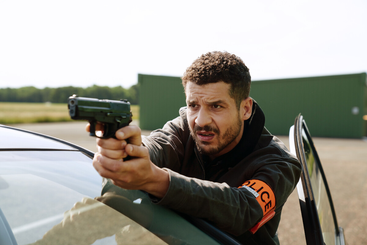 Soufiane Guerrab as Youssef Guedira holds a gun in Season 3 of ‘Lupin.’