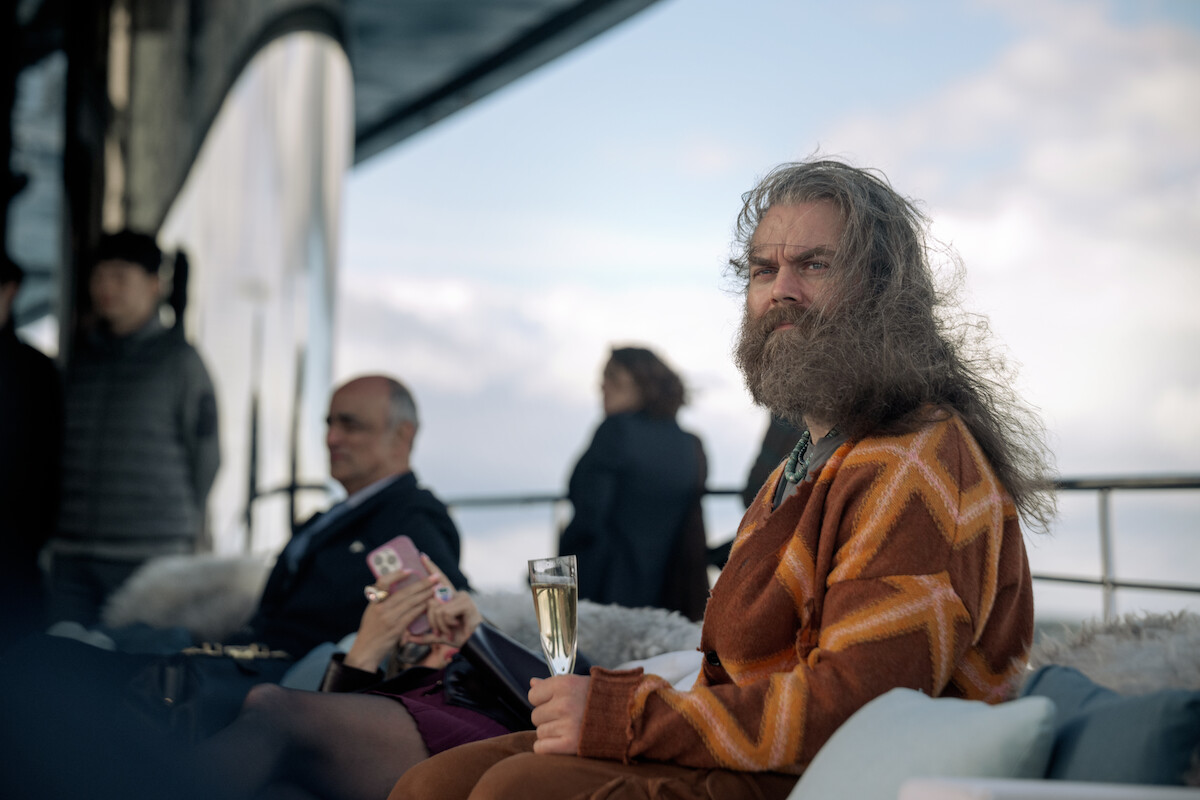 A bearded Christopher Rygh holds a champagne flute aboard the deck of a yacht.