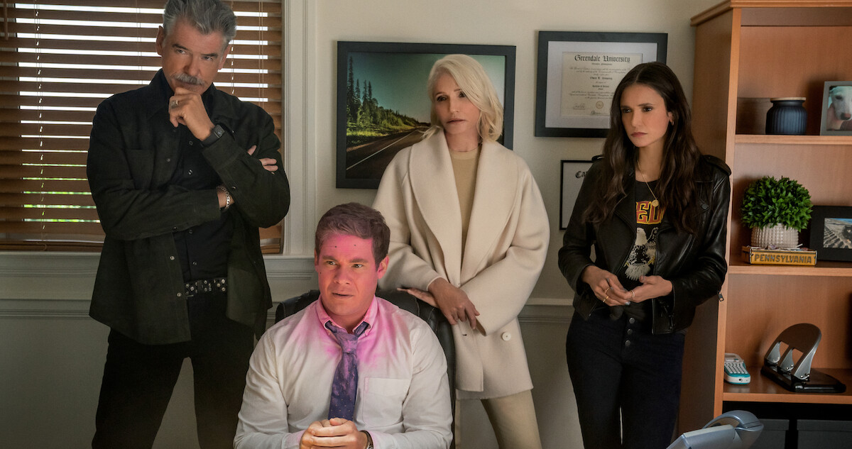 Pierce Brosnan, Ellen Barkin and Nina Dobrev stand behind Adam Devine with pink paint on his face in a still from ‘The Out-Laws.’