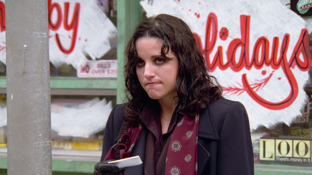 Elaine looks exasperated while holding a business card.