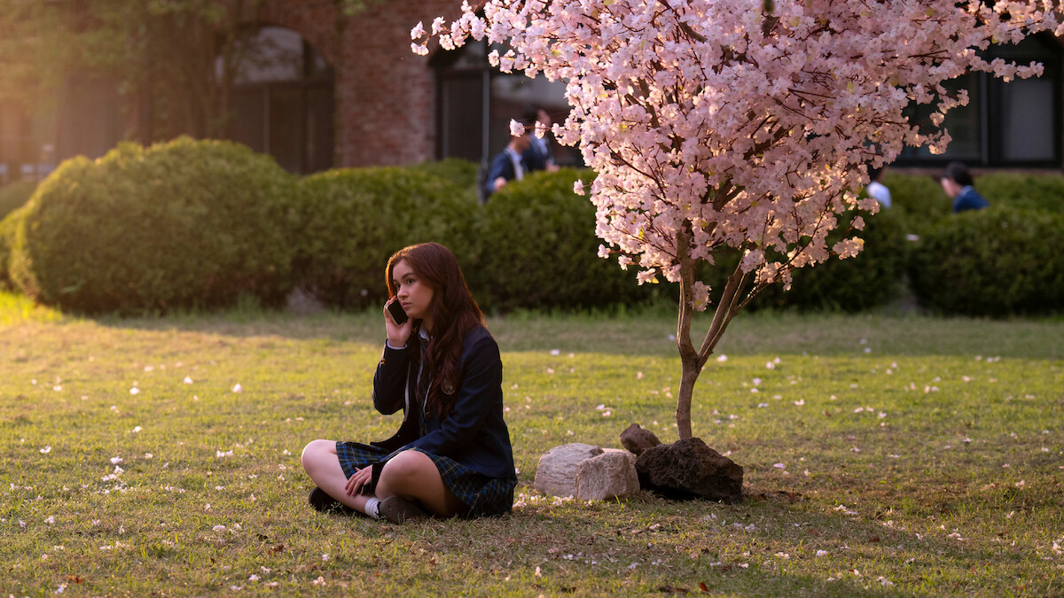 Anna Cathcart as Kitty Song Covey sits under a tree with pink blossoms in Season 2 of 'XO, Kitty' 