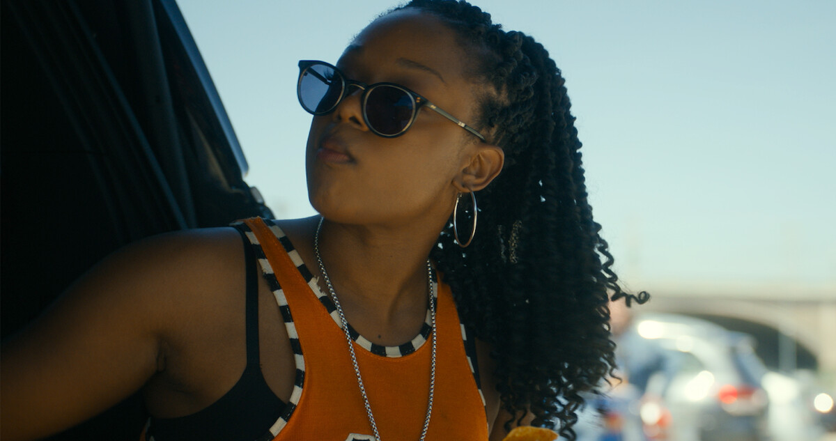 A woman in sunglasses and a bright top looks off to the side.
