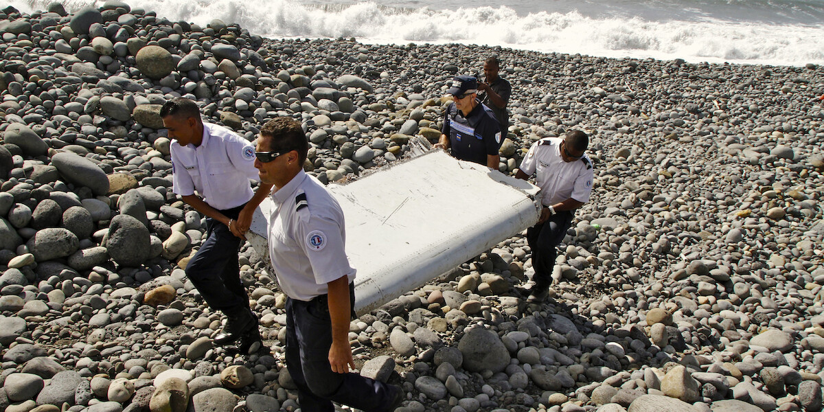 A team of officials on a rocky beach carry what looks like part of a plane wine.