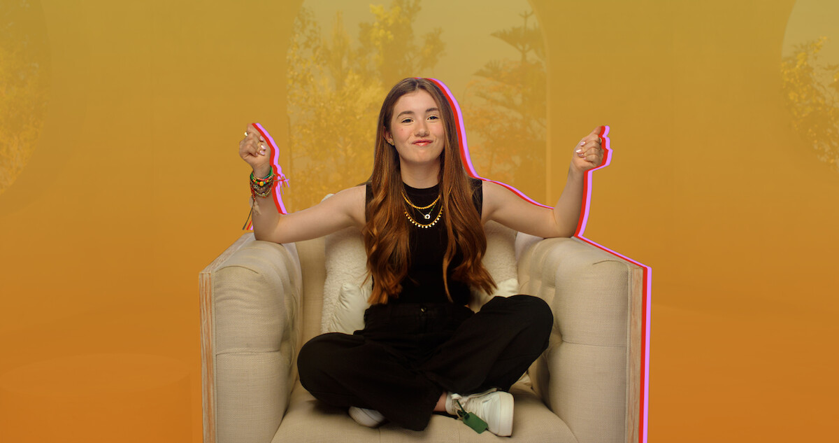 Lucy Paez sits on a couch against a yellow backdrop.