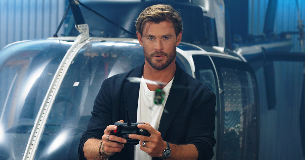 Chris Hemsworth holds a remote control in front of a helicopter in a still from an 'Extraction 2' promo video. 
