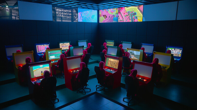Several Squid Game guards sitting at a computer terminal monitoring the games. 