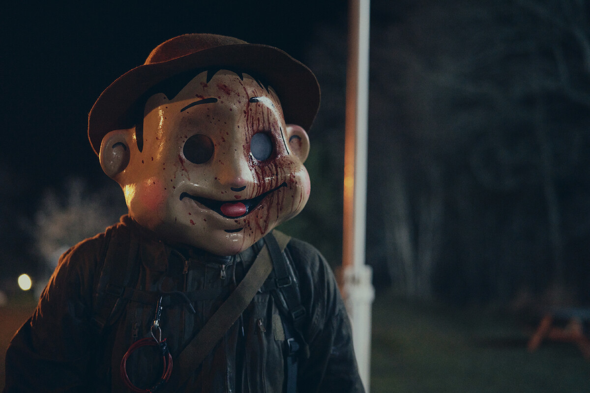 A man wearing a large, cartoonish mask of a boy’s face in ‘The Conference’