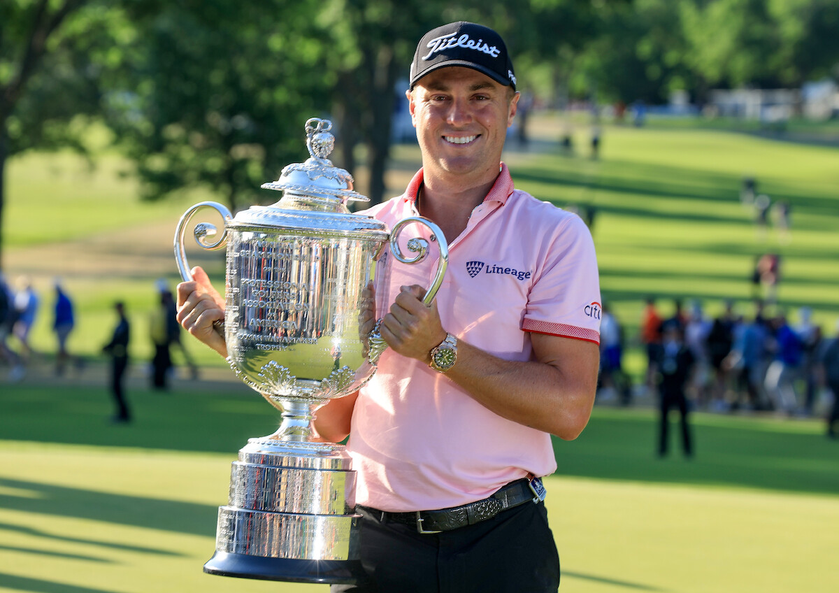 Golfer Justin Thomas holding a large silver trophy. 
