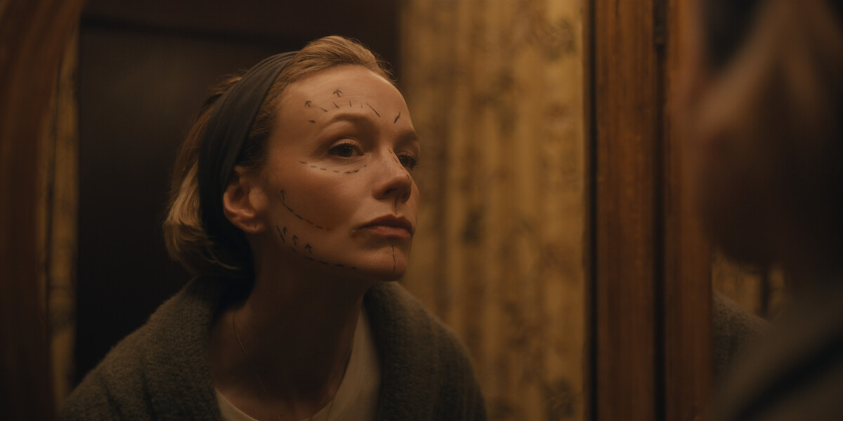 Woman with facial markings looking at herself in a mirror in a dimly lit, vintage-style bathroom, wearing a headband and sweater, thoughtful expression.