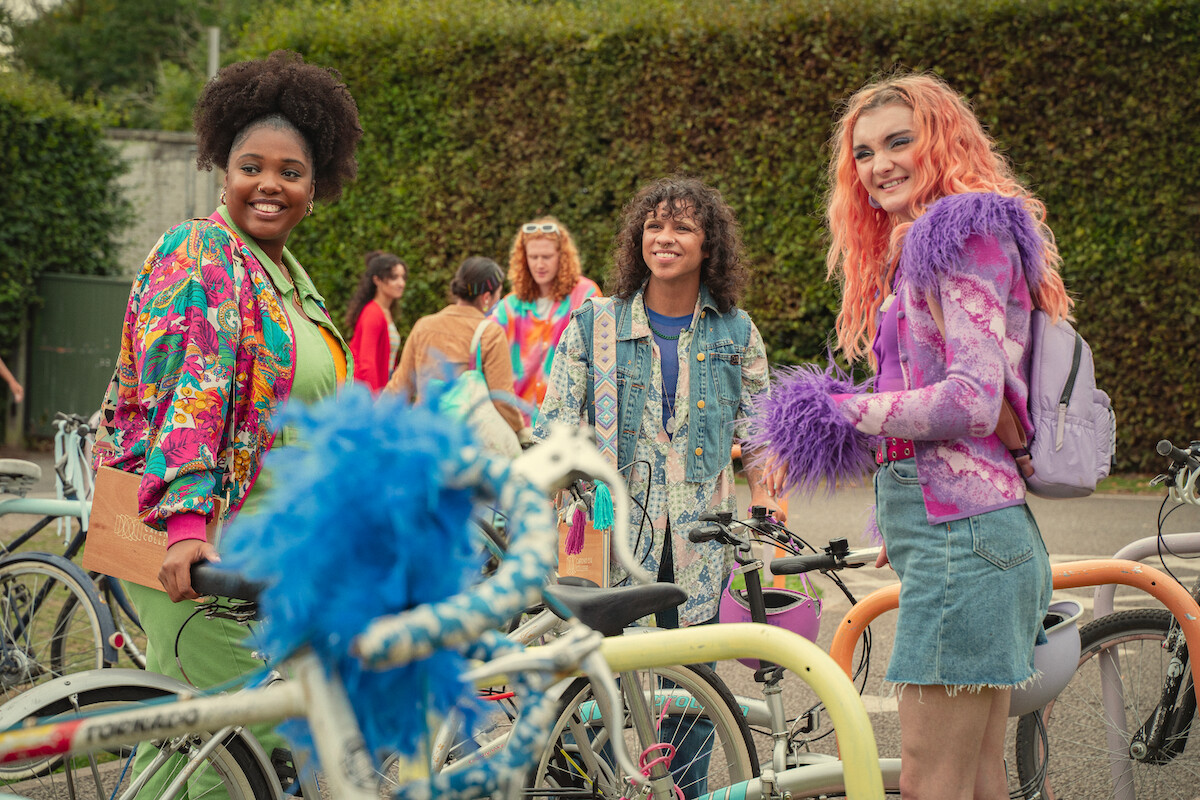 Alexandra James as Aisha, Felix Mufti as Roman, and Anthony Lexa as Abbi stand together smiling outside of school in Season 4 of 'Sex Education.'