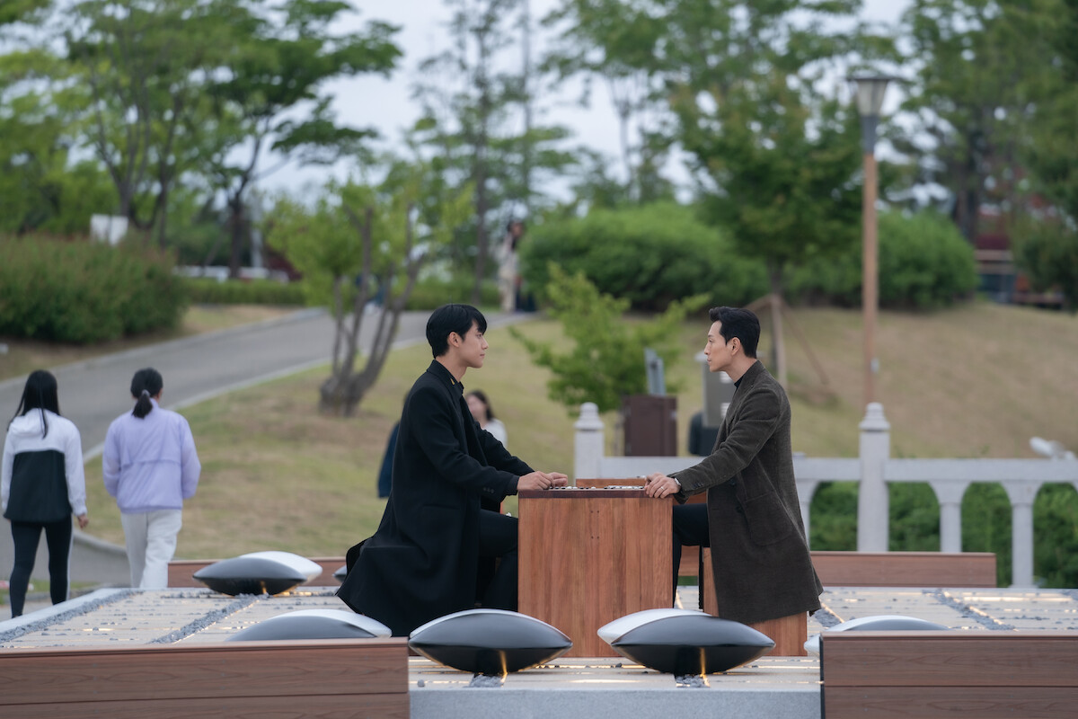 Two characters sitting opposite one another in a park playing Go.