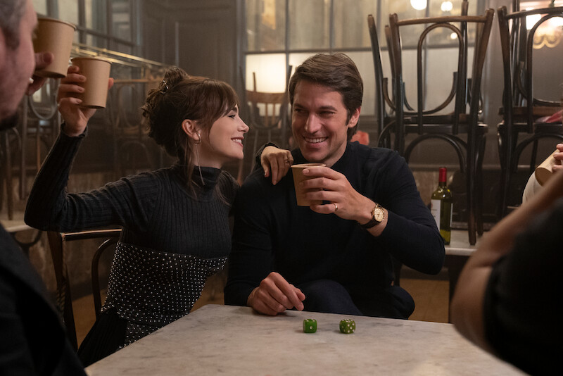 Lily Collins as Emily and Lucas Bravo as Gabriel laugh together at a restaurant in Season 4 of 'Emily in Paris'