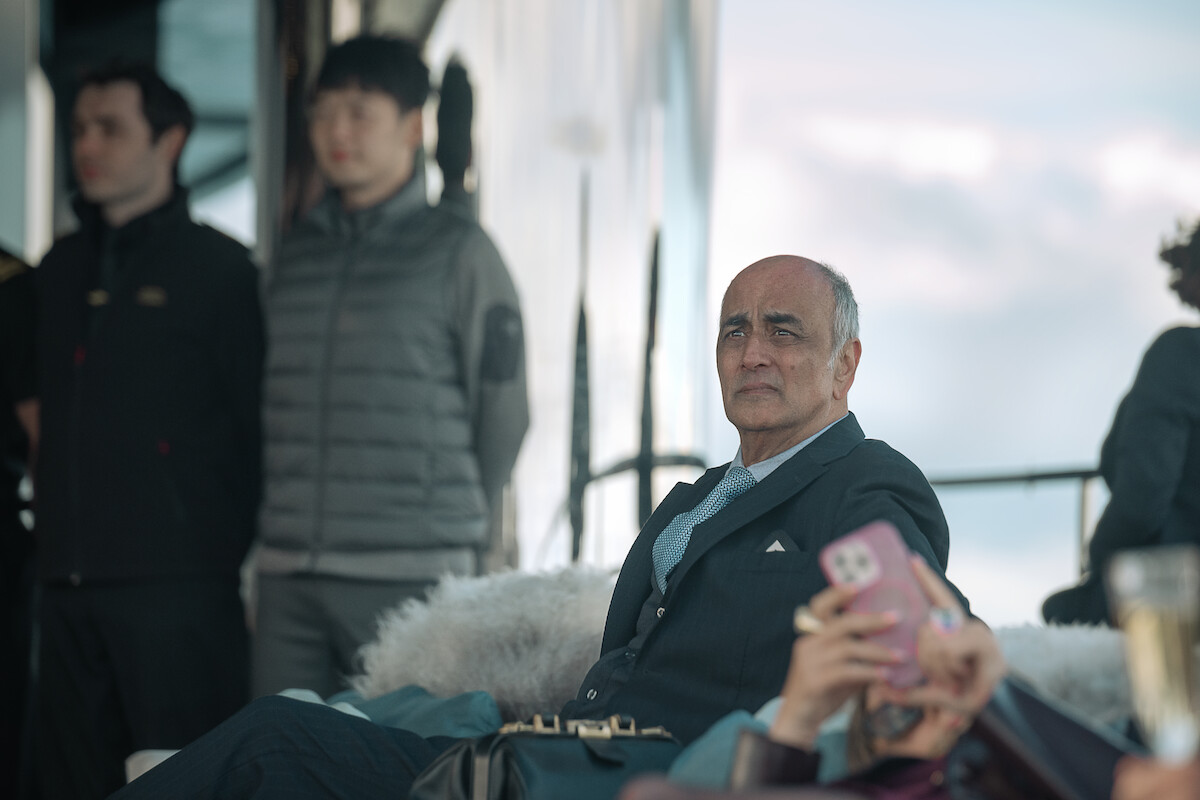 Art Malik sits aboard the deck of a yacht with a concerned expression on his face.